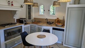 Una cocina moderna con estufa a gas, horno y lavavajillas. Hay una mesa redonda con un posavasos de madera, sillas negras y una lámpara colgante.