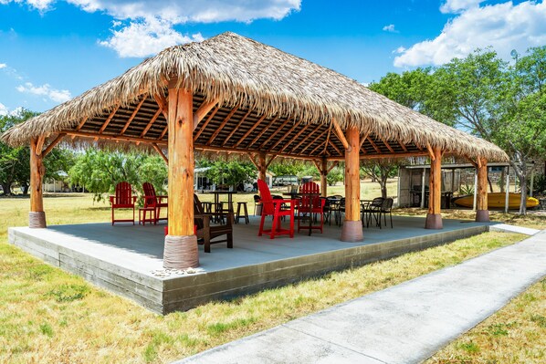 A wooden pavilion with a thatched roof, surrounded by outdoor seating and tables.