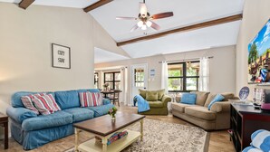 A spacious living room with a high ceiling, a ceiling fan, and a large window.