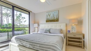 Ein Schlafzimmer mit einem großen Bett, einem Nachttisch mit Lampe, einem Bild an der Wand und Blick ins Grüne durch eine Schiebetür.
