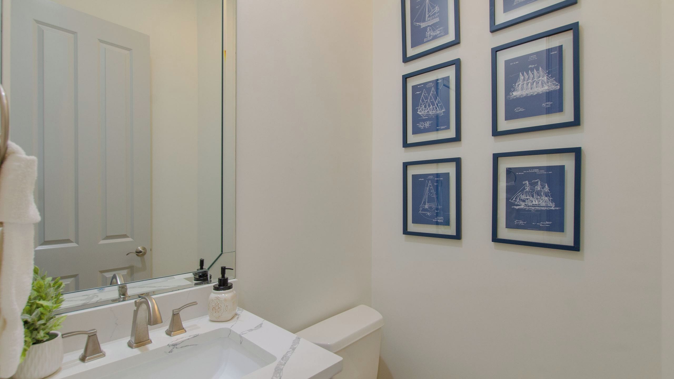 A bathroom with a white sink, a mirror, a toilet, and framed blue nautical drawings on the wall.