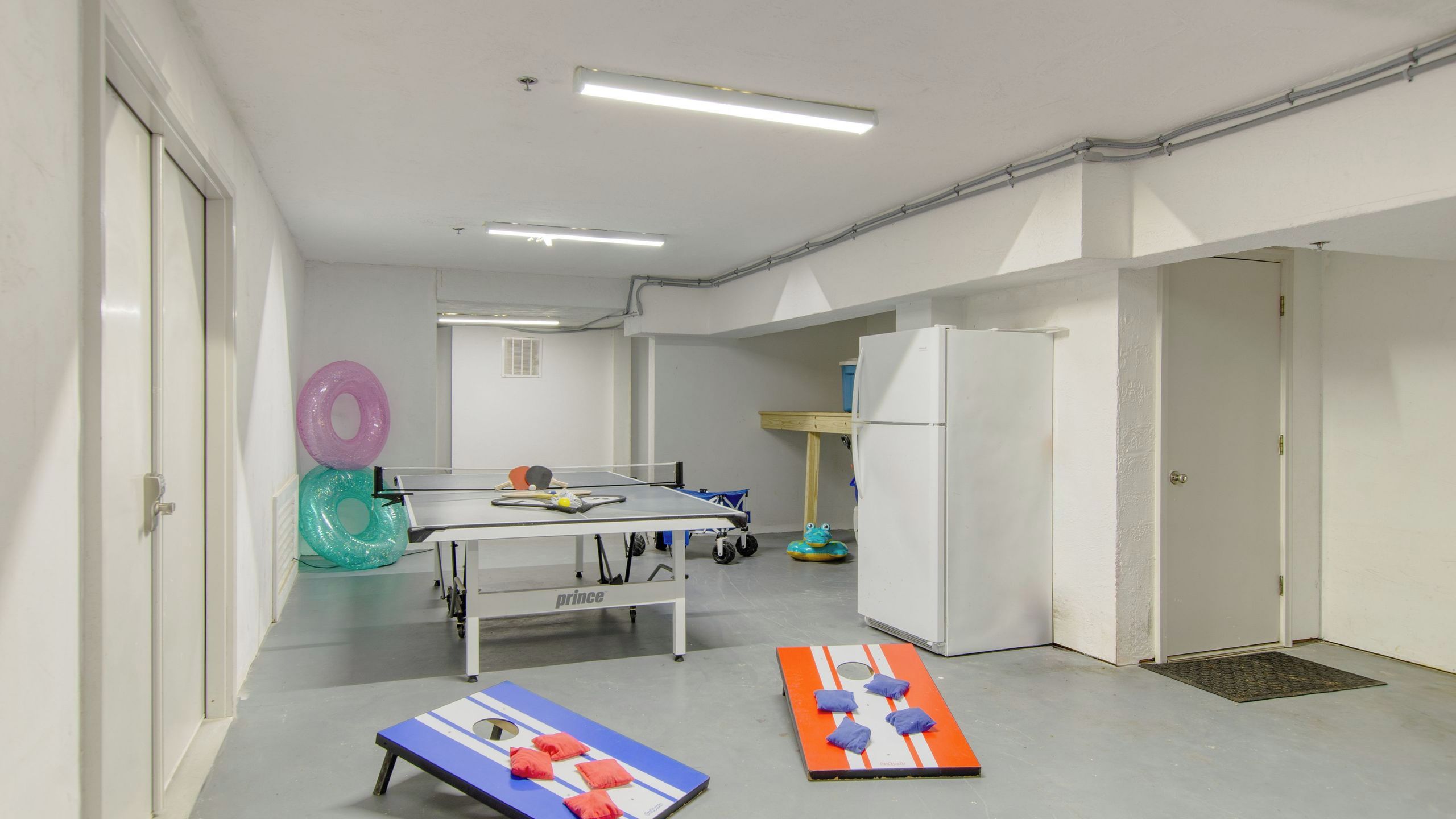 Una stanza con tavolo da ping pong, attrezzature per esercizi e un frigorifero.