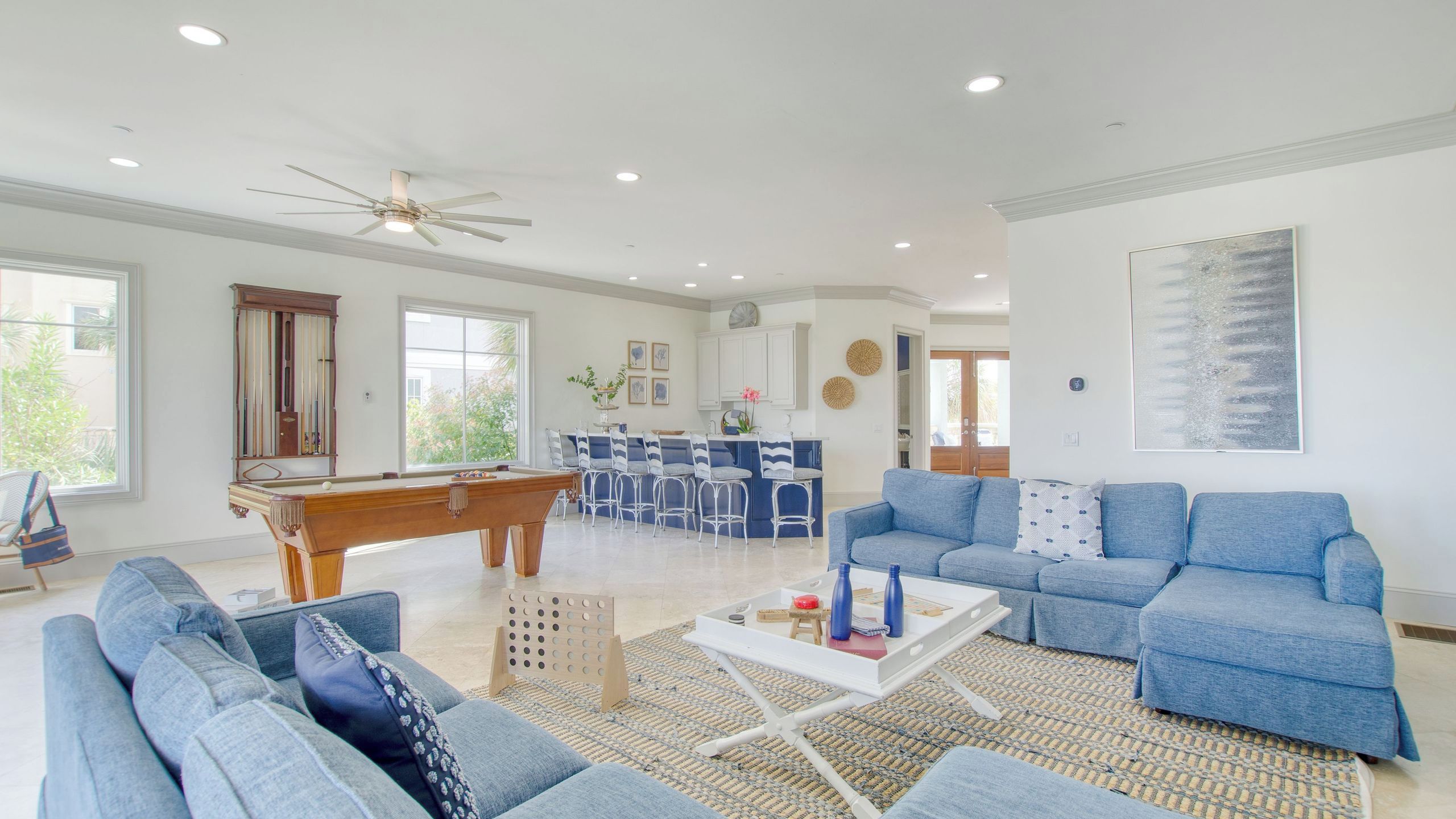 A spacious living room with a pool table, blue sofas, and a ceiling fan.