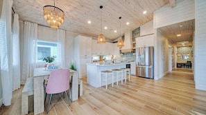 A spacious kitchen with wooden flooring, white cabinetry, and a central island with bar stools. - Private Pool, Firepit, Balcony, Patio Boat Parking Mint to Be by Avantstay (Port Aransas)