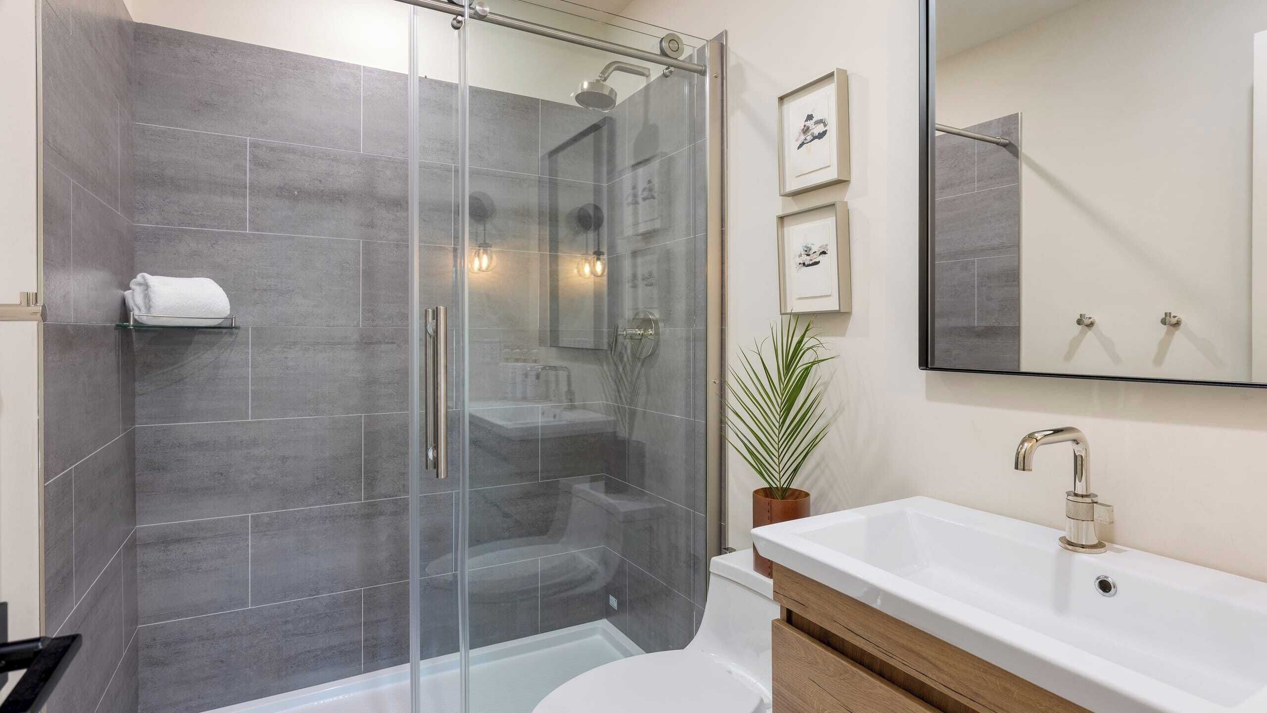A modern bathroom with a glass-enclosed shower, a white sink, and a large mirror.