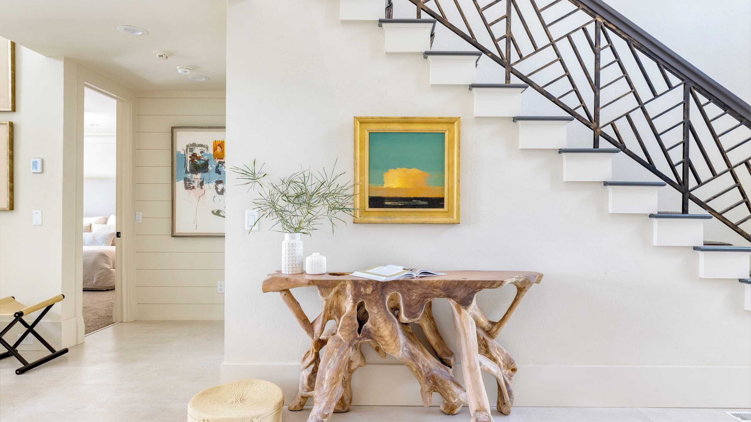 A modern interior with a staircase, a wooden console table, and a framed painting.