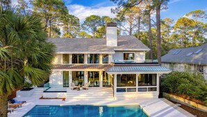 Une maison moderne à deux étages, dotée d’une grande façade vitrée, d’une piscine et d’un patio couvert.