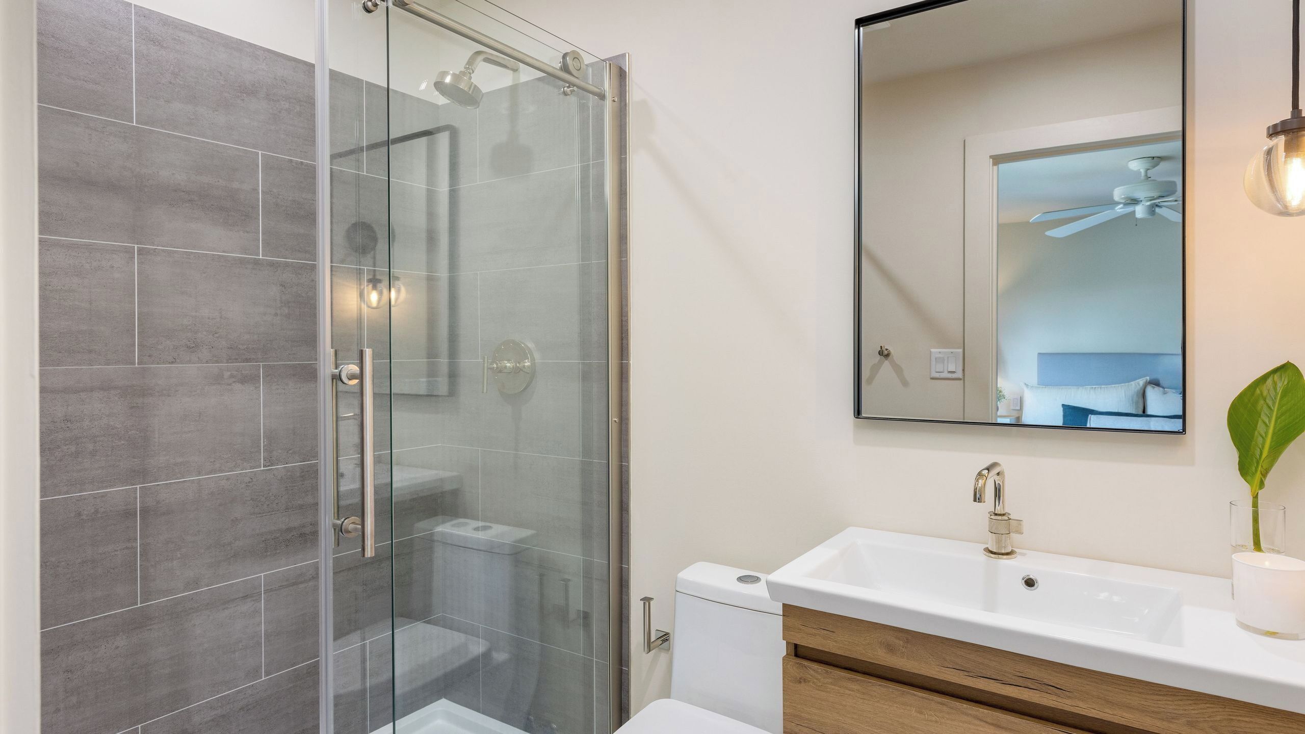 A modern bathroom with a glass-enclosed shower, a white sink, and a large mirror.
