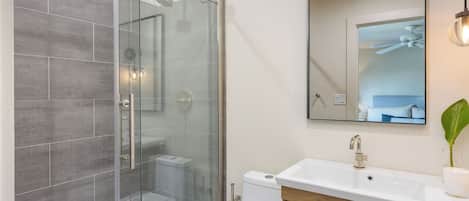 A modern bathroom with a glass-enclosed shower, a white sink, and a large mirror.