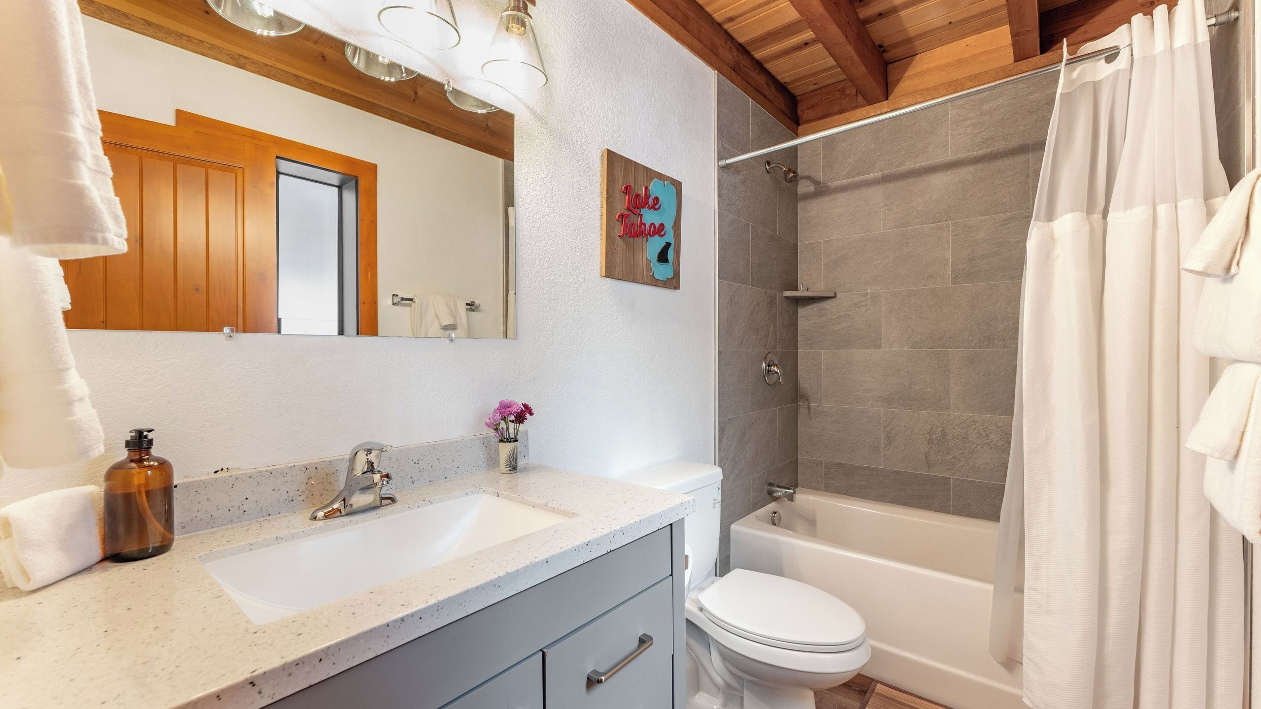 Un baño con ducha, inodoro, lavamanos y espejo.
