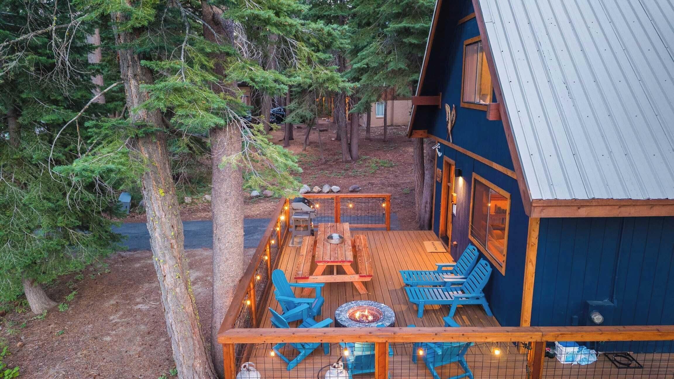 A wooden deck with a fire pit, outdoor seating, and a view of a forested area.