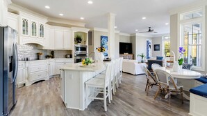 Une cuisine spacieuse avec des meubles blancs, un îlot central et un coin repas doté de chaises en osier.