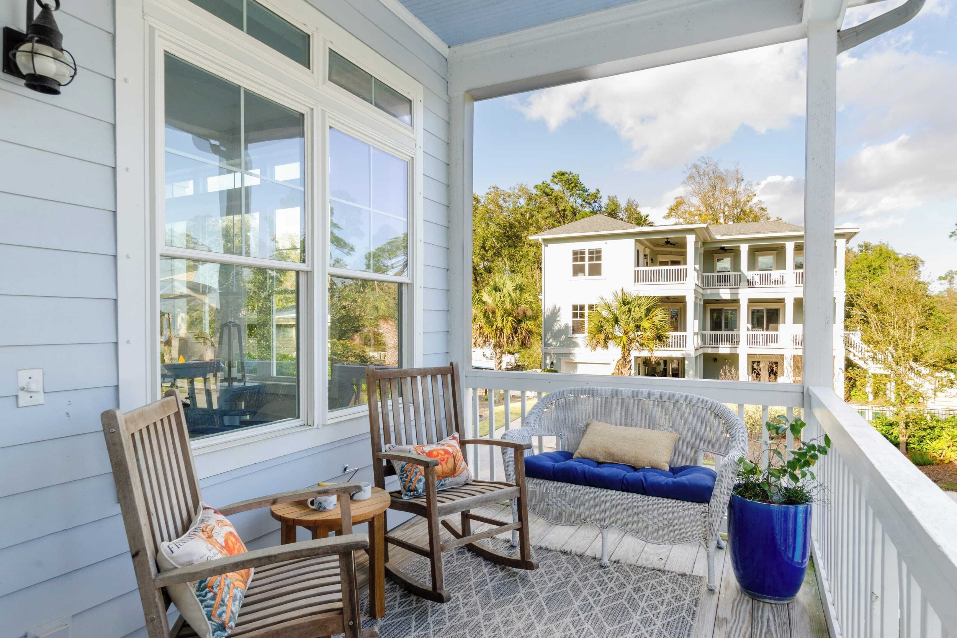 A covered porch with wicker furniture, a rocking chair, and a blue potted plant.