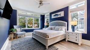 A bedroom with a bed, nightstands, a chair, a ceiling fan, and large windows. - Steps to Beach Pool, Hot Tub, Fire Pit 7br, Sleeps 18 Cobalt Coast (Hilton Head Island)