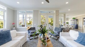 A spacious living room with white sofas, a coffee table, and a glass-top table with plants.