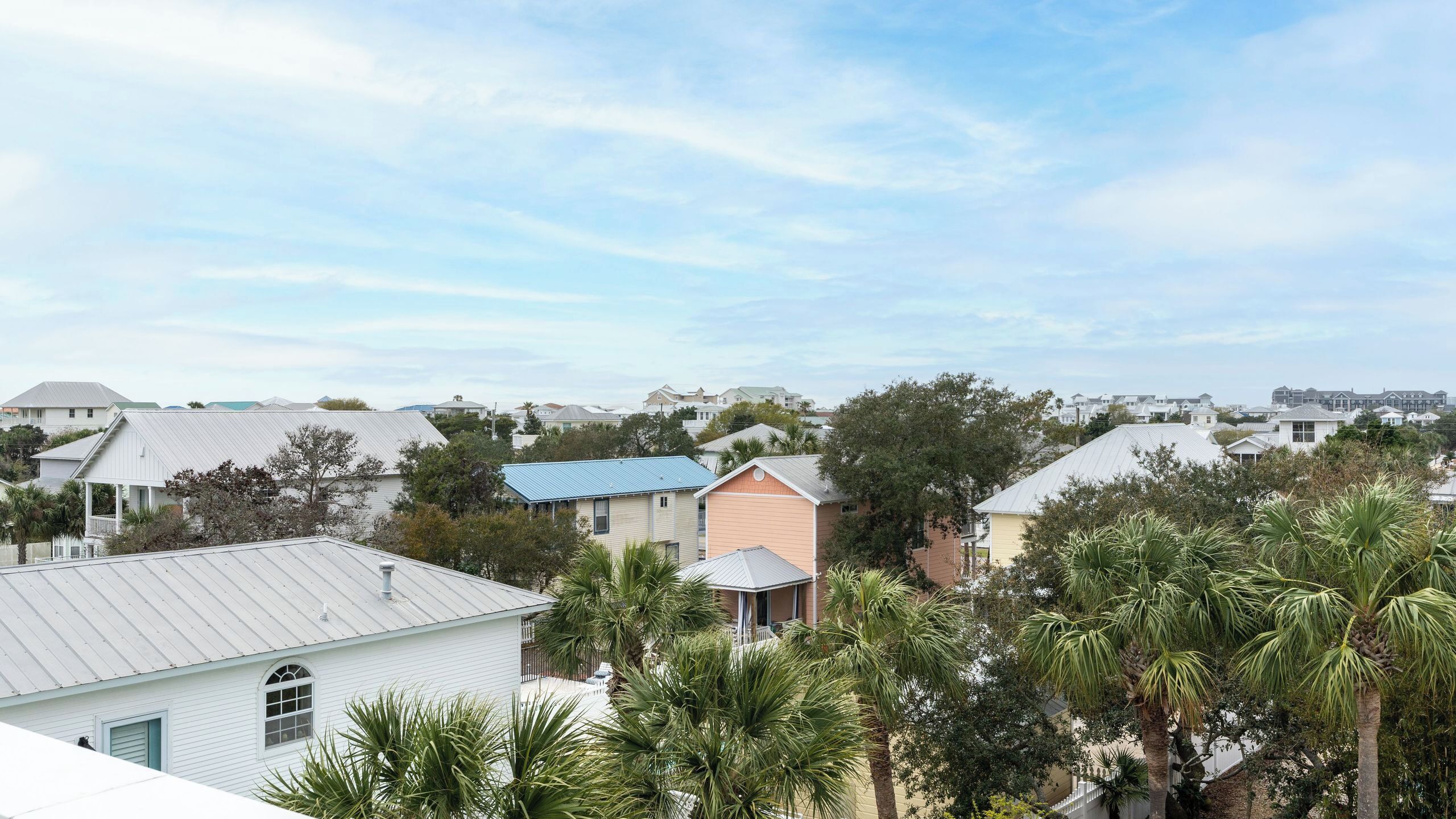 A residential area with houses, some with blue roofs, surrounded by palm trees.
