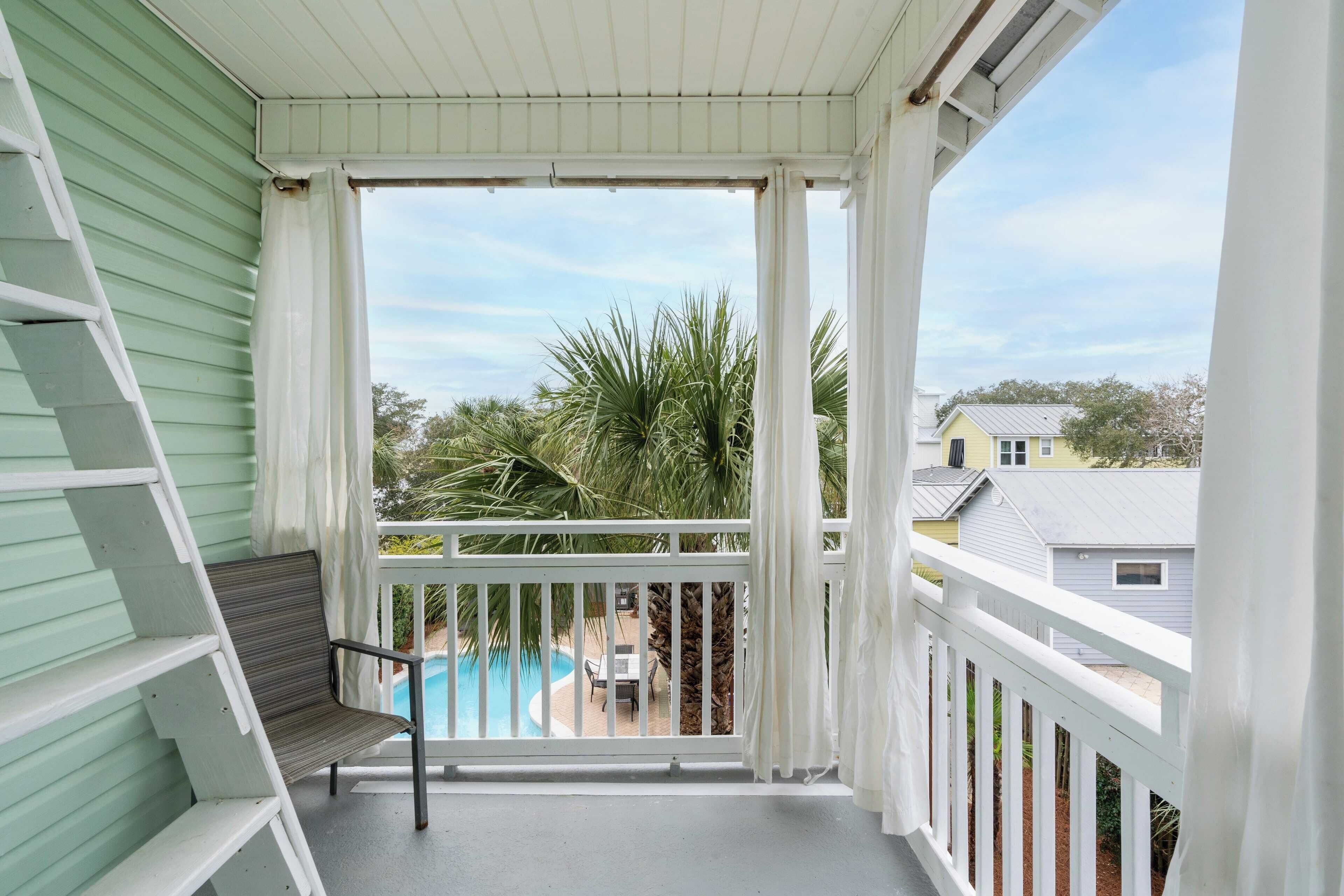 Un balcon avec vue sur une piscine, des palmiers et les maisons voisines.
