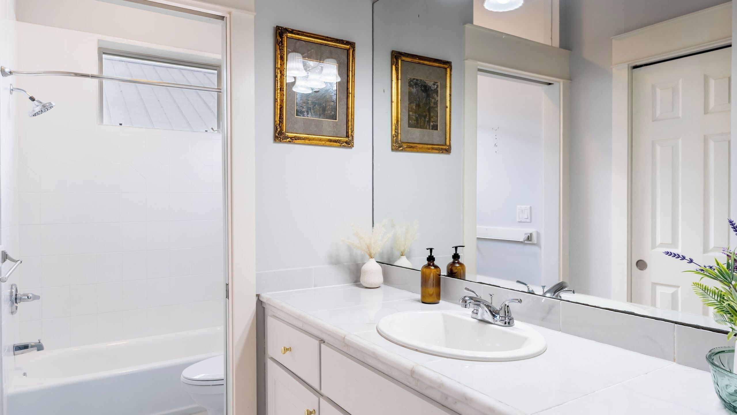 Une salle de bain avec une baignoire, un lavabo, un miroir et des tableaux encadrés au mur.