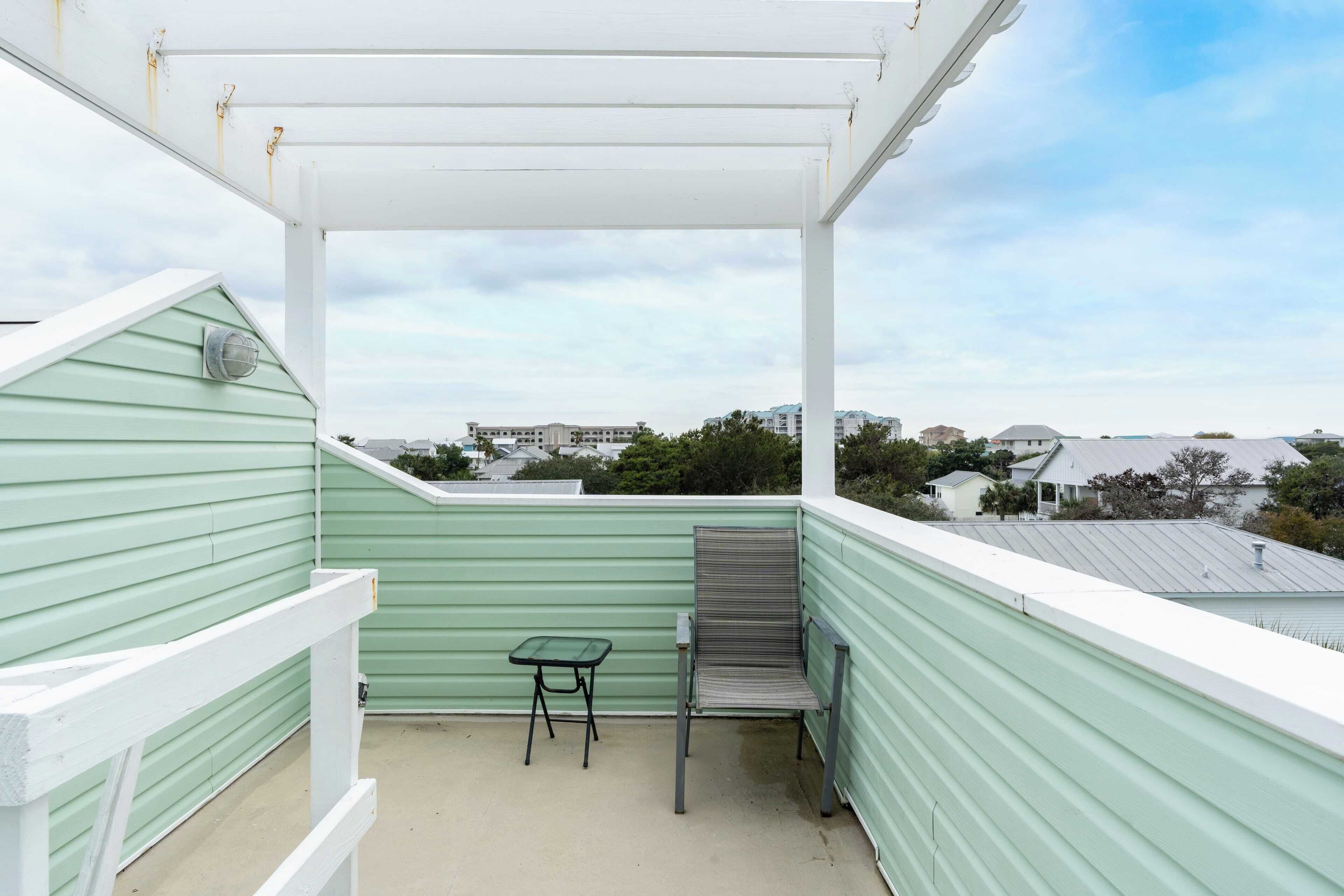 A balcony with a green railing, a white pergola, a small table, and a chair.