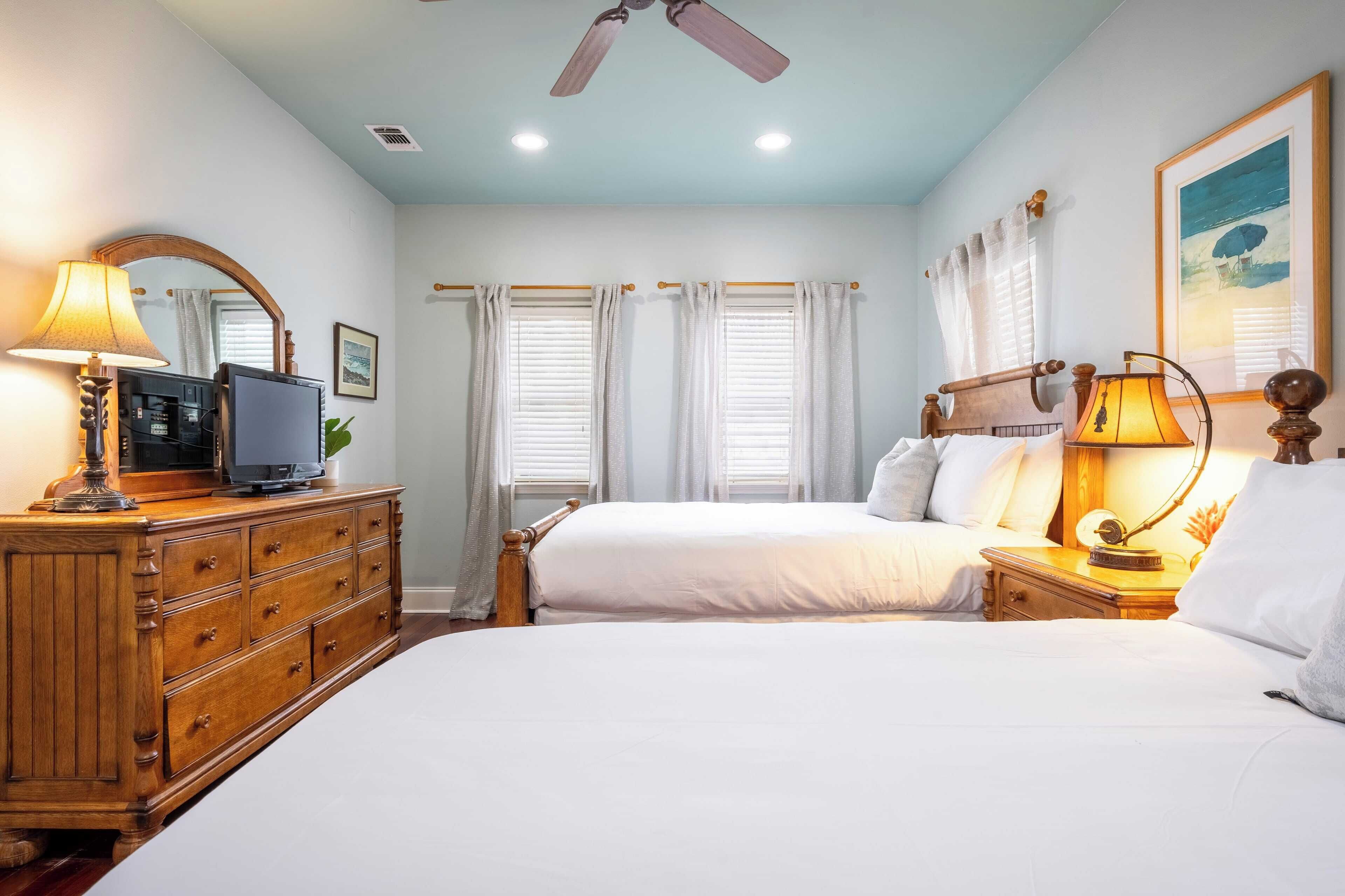 A bedroom with a bed, dresser, TV, and ceiling fan.