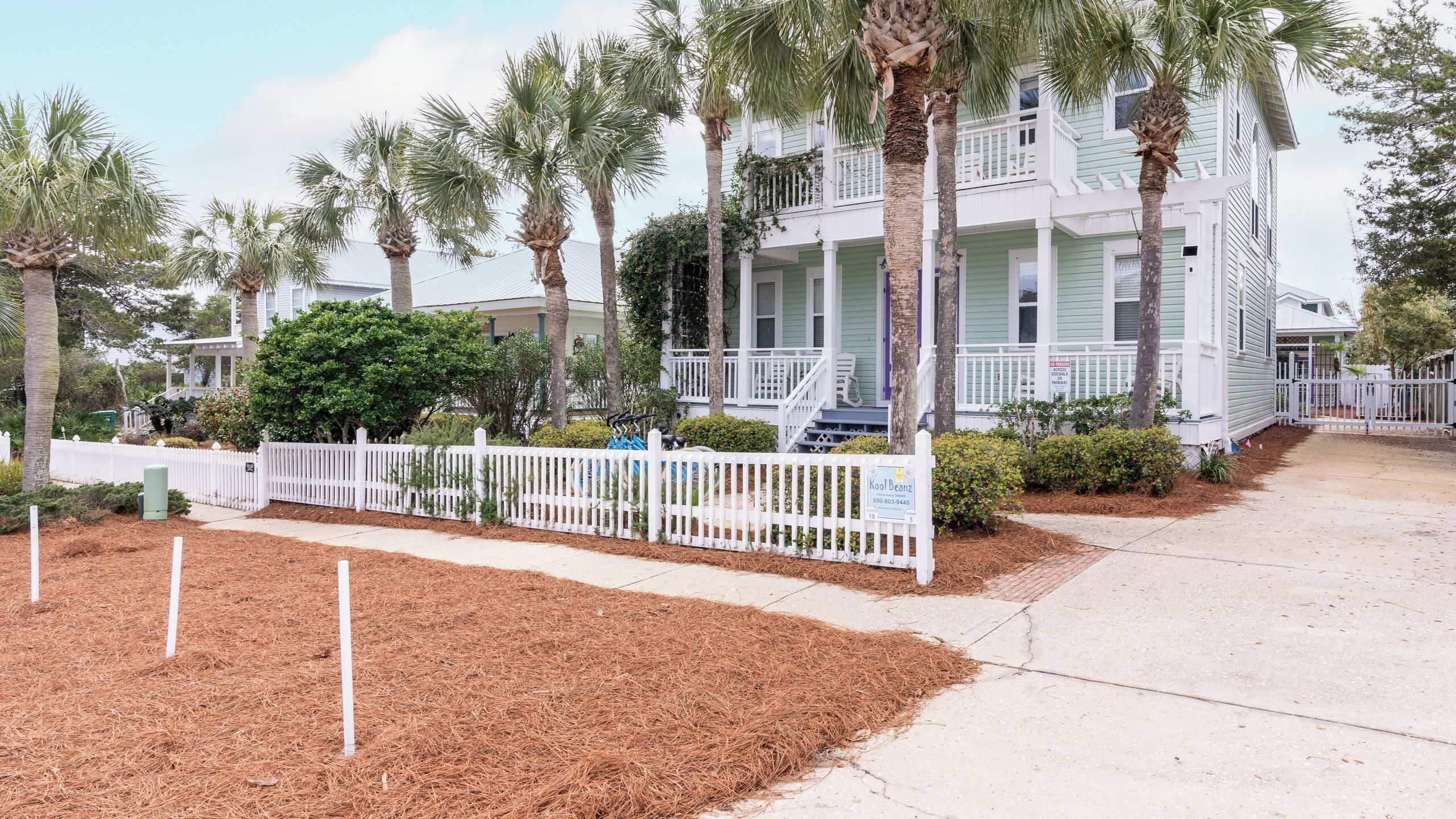 A beachfront property with a white fence, palm trees, and a light green building with a balcony.