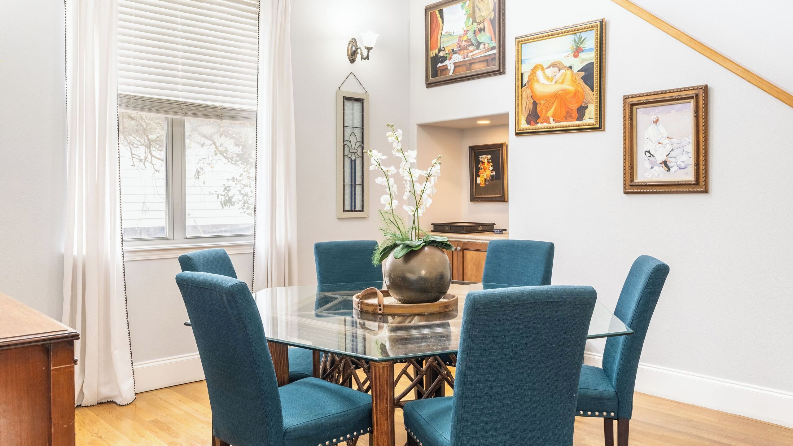 A dining area with a glass table, blue upholstered chairs, and a vase with white flowers.