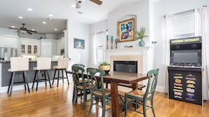 A dining area with a wooden table and chairs, a fireplace, and a gaming console. - Kool Beanz by Avantstay Private Pool, Near Beach (Destin)