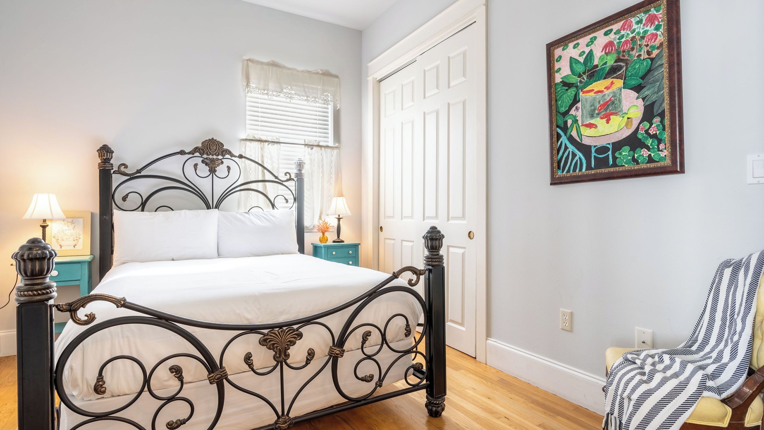 A bed with a metal frame, a nightstand with a lamp, a door, and a wall with a painting.