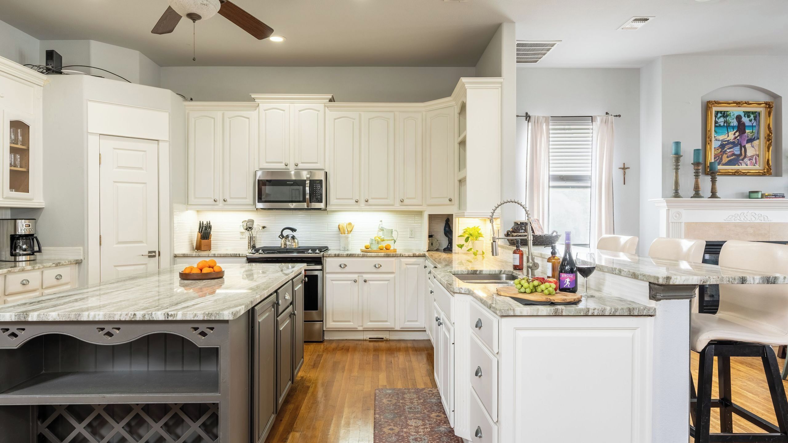 A kitchen with white cabinets, a microwave, a sink, and a dining area with a bar stool.