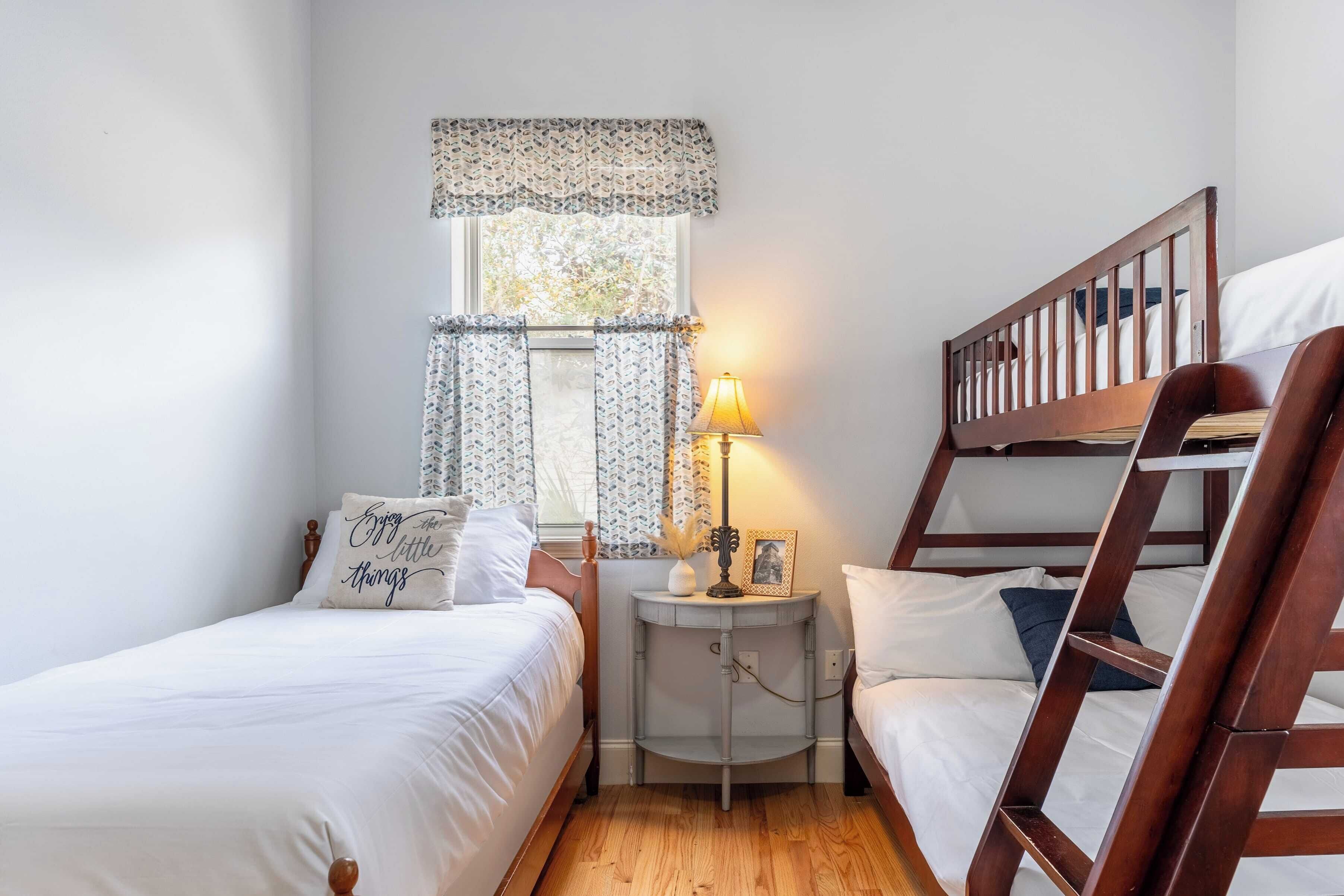 Une chambre avec deux lits simples, une table de chevet avec une lampe et une fenêtre agrémentée de rideaux à motifs.