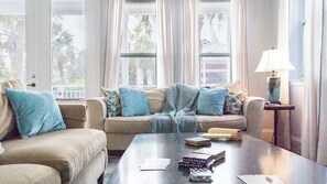 A living room with a sofa, a coffee table with books and a lamp, and a window with curtains. - Kool Beanz by Avantstay Private Pool, Near Beach (Destin)