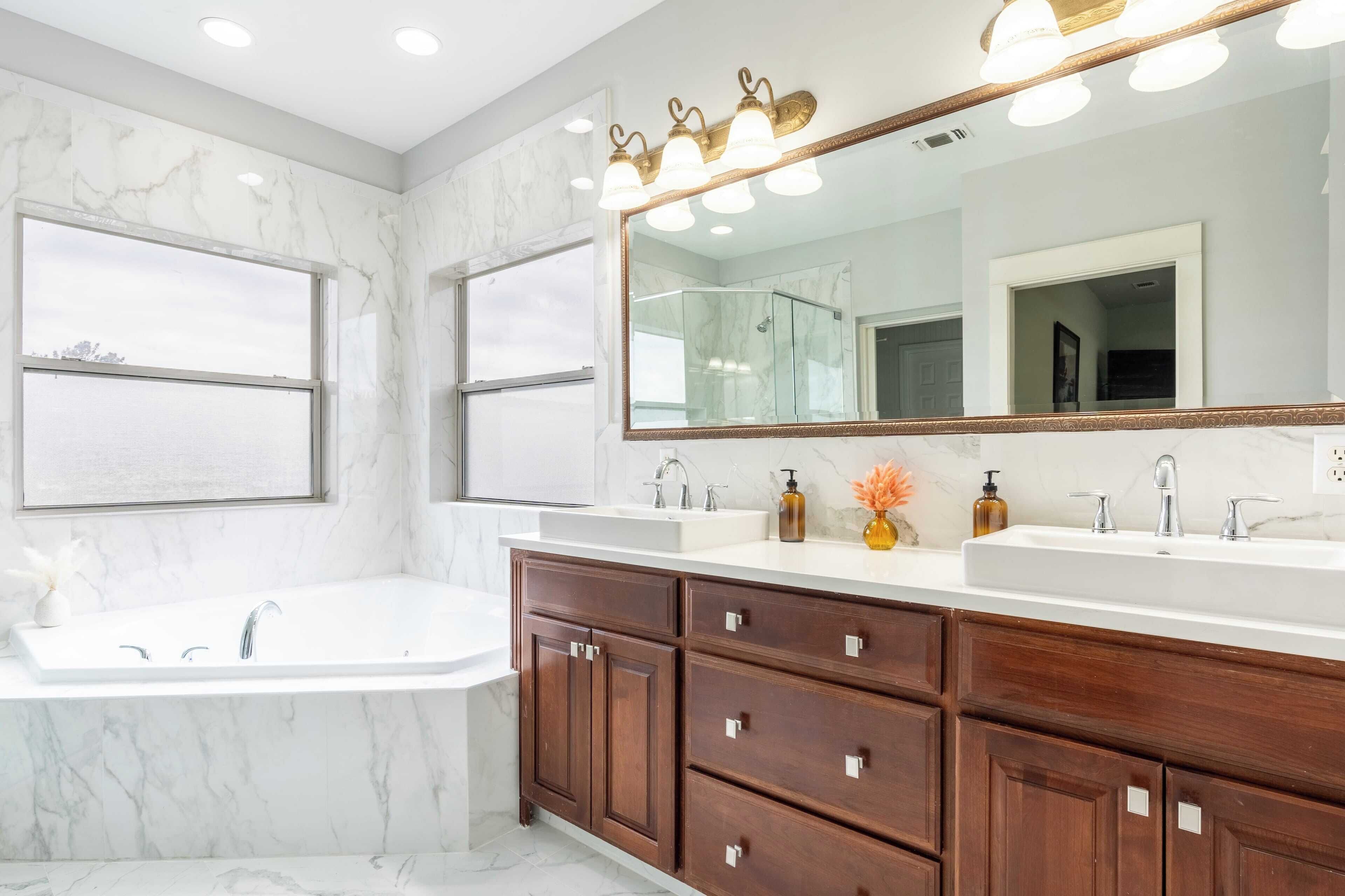 A modern bathroom with a large mirror, dual sinks, and a bathtub.