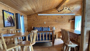 A wooden cabin interior with a dining table, chairs, a sofa, and a chandelier. - Galena Road Cabins (Deadwood)