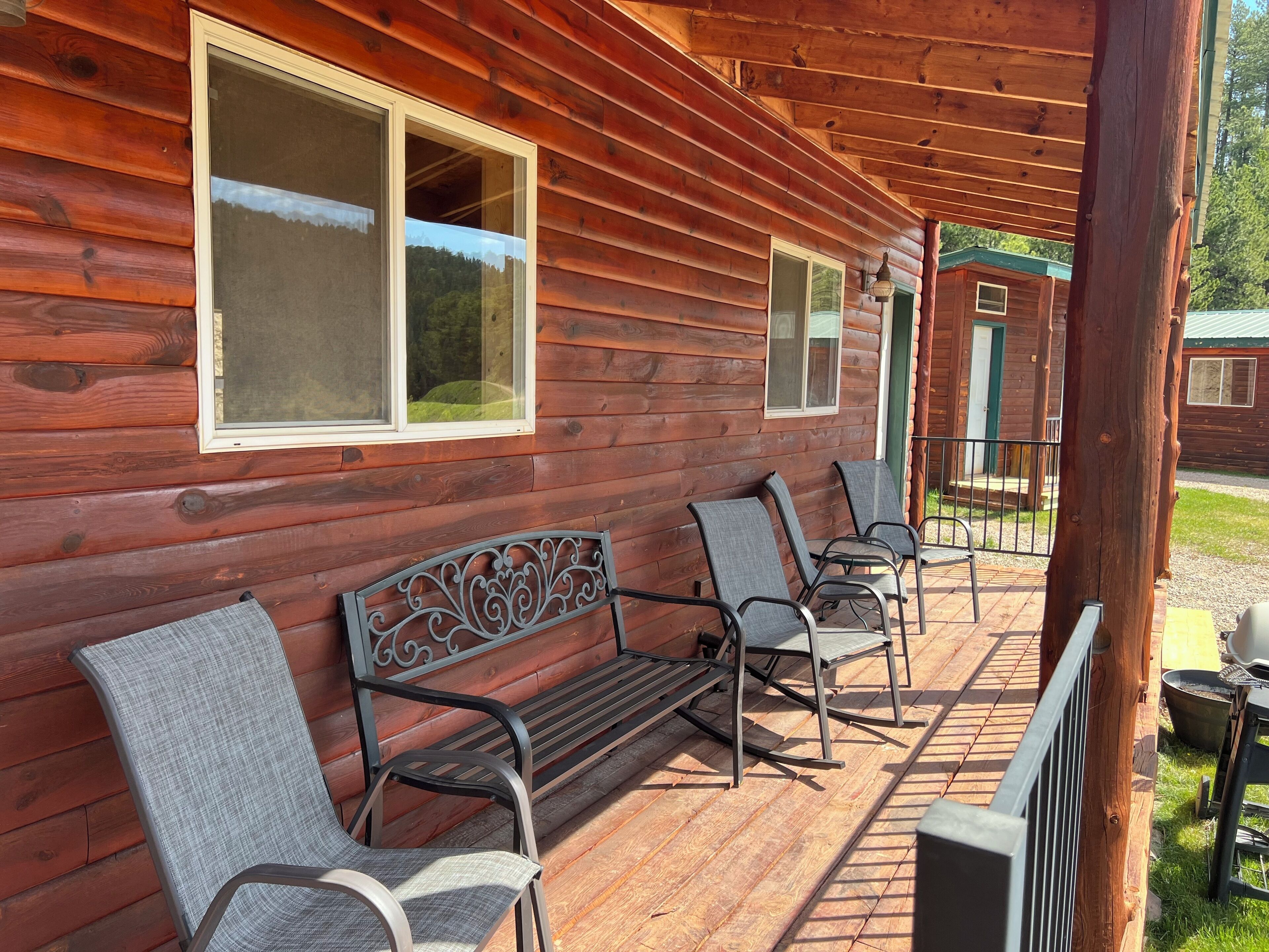 A wooden cabin with a porch featuring a bench and four chairs.