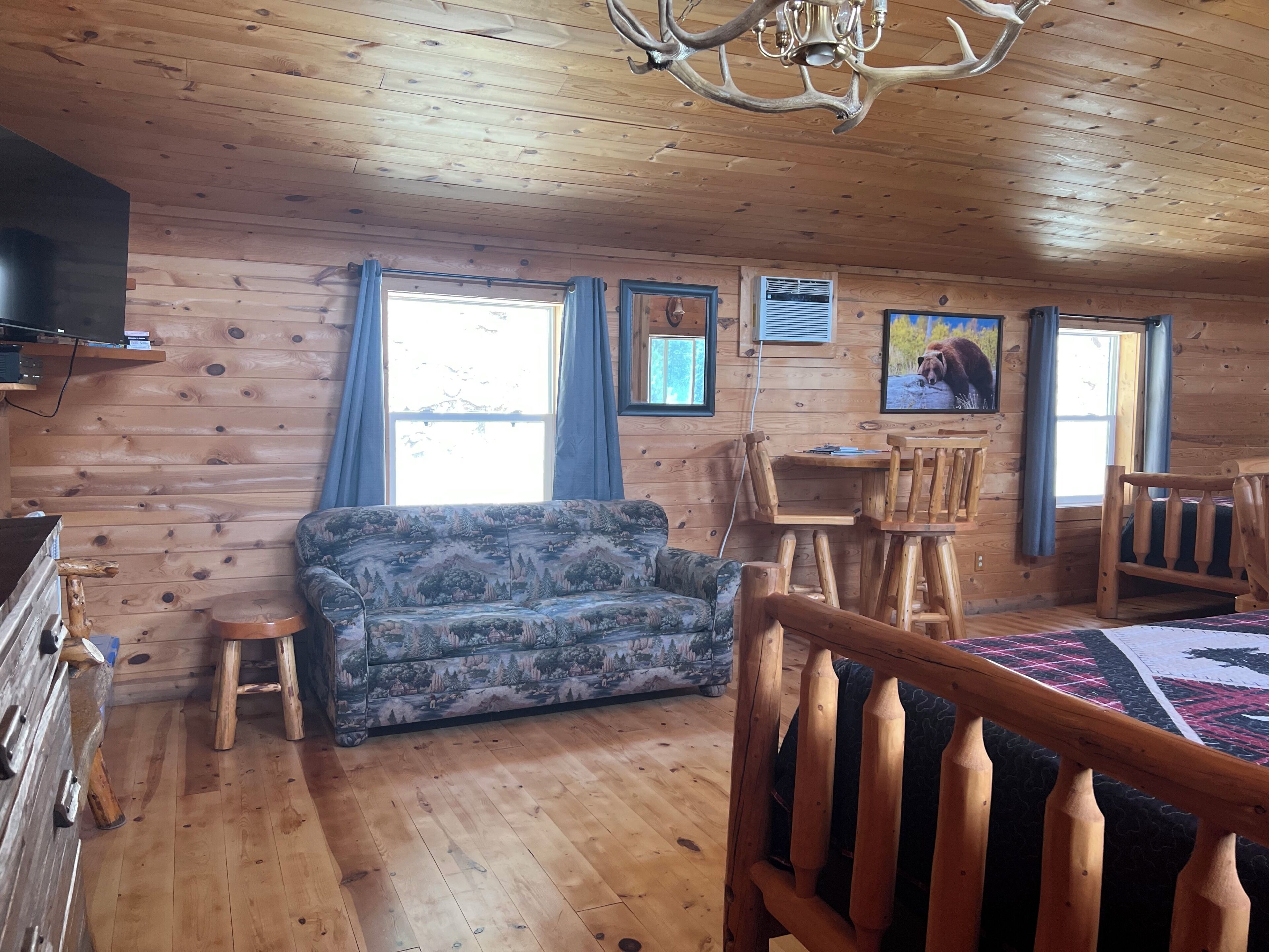 Ein Holzblockhaus-Innenraum mit einer Couch, einem Esstisch, Stühlen und einem Fernseher.