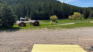 A rural landscape with a gravel area, wooden cabins, and a forested hill. - Galena Road Cabins (Deadwood)