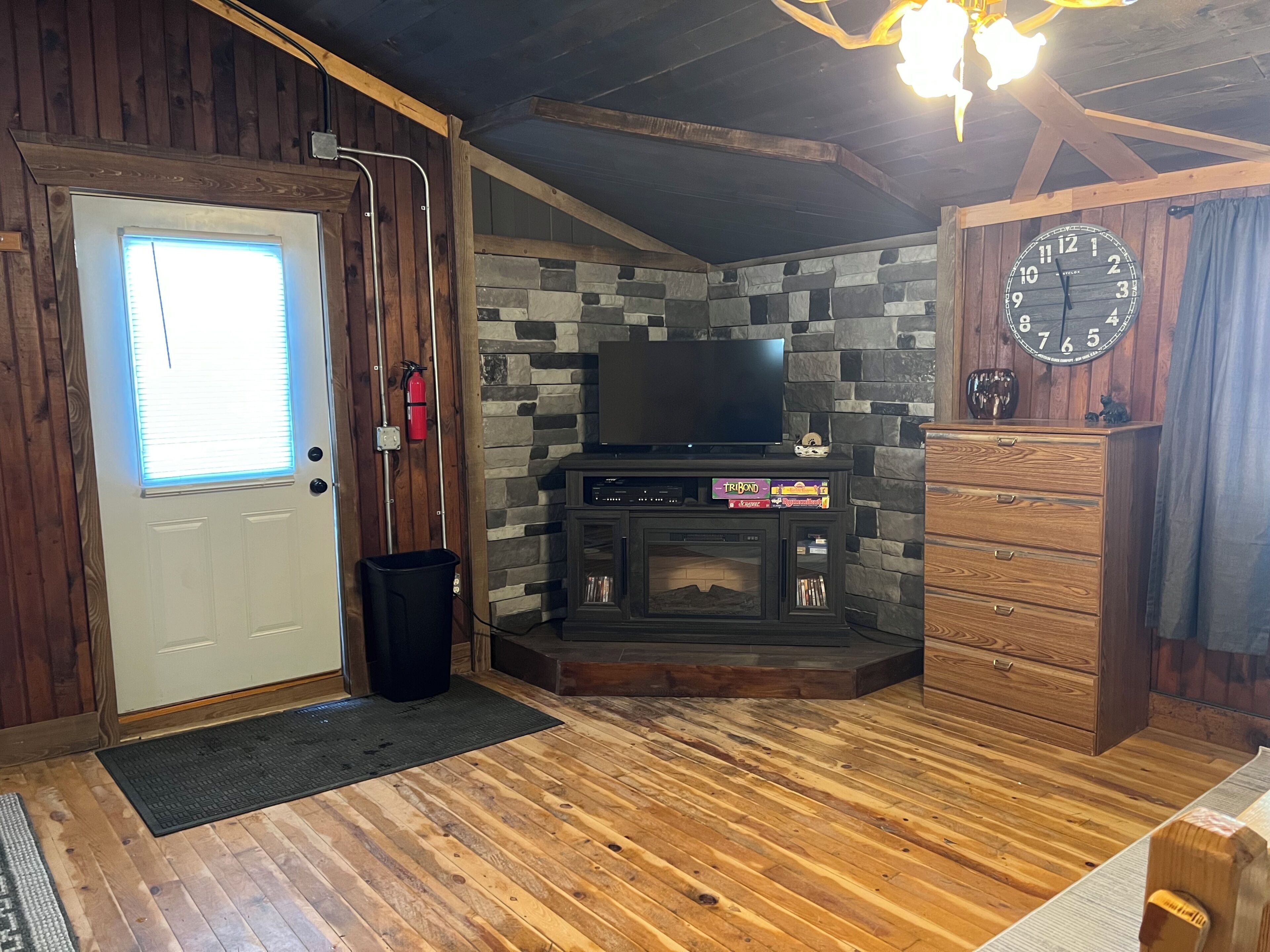 A wooden interior with a stone wall, a fireplace, a television, and a clock.