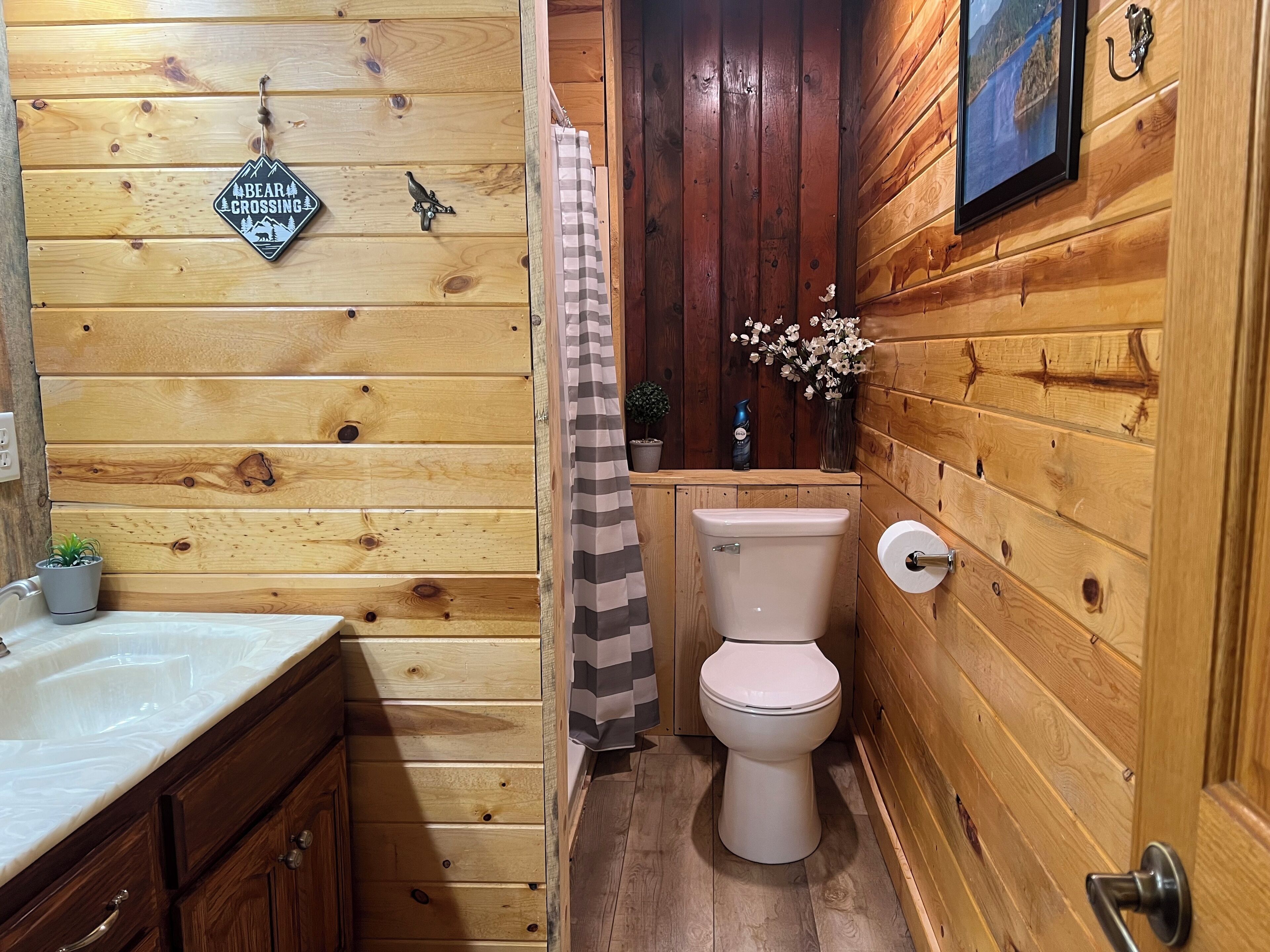 A wooden cabin bathroom with a toilet, sink, and shower curtain.
