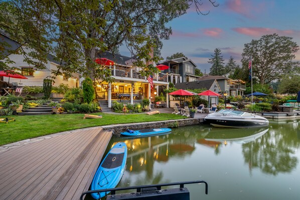 A waterfront property with a wooden dock, a boat, and a building with outdoor seating and umbrellas. - {Lake Front Fun} The Little Cottage on West Bay of Lake Oswego (Lake Oswego)