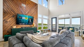 Ein modernes Wohnzimmer mit großem Flachbildfernseher, einem modularen Sofa und Blick ins Freie durch große Fenster.