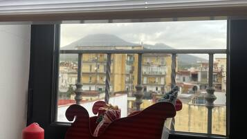 Una finestra con un giocattolo a forma di slitta rossa sul davanzale, una candela rossa e una vista di un paesaggio urbano con edifici e una montagna all'orizzonte.