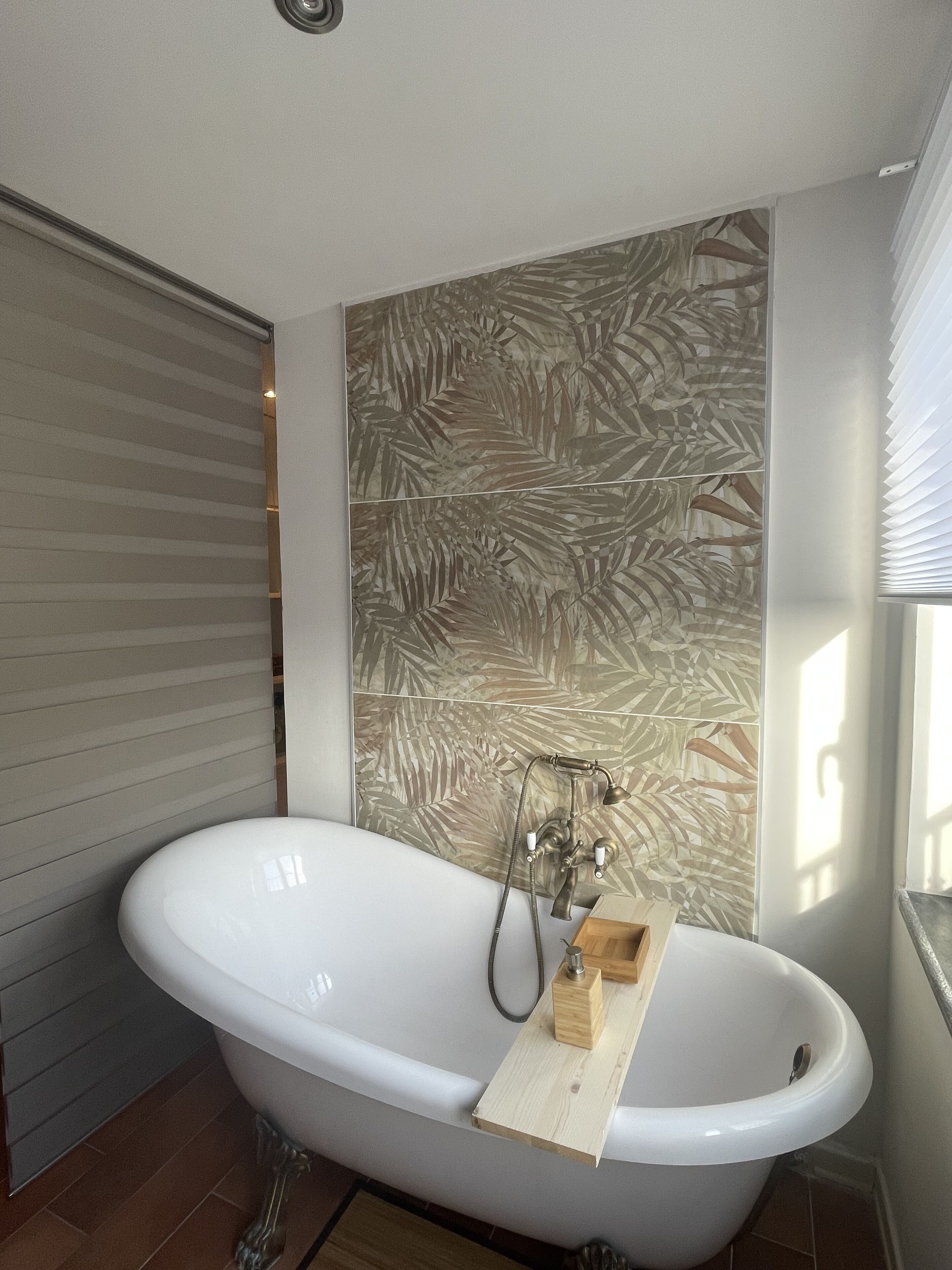 Une salle de bain avec une baignoire sur pieds, un plateau en bois et un mur orné d’un motif de feuilles.