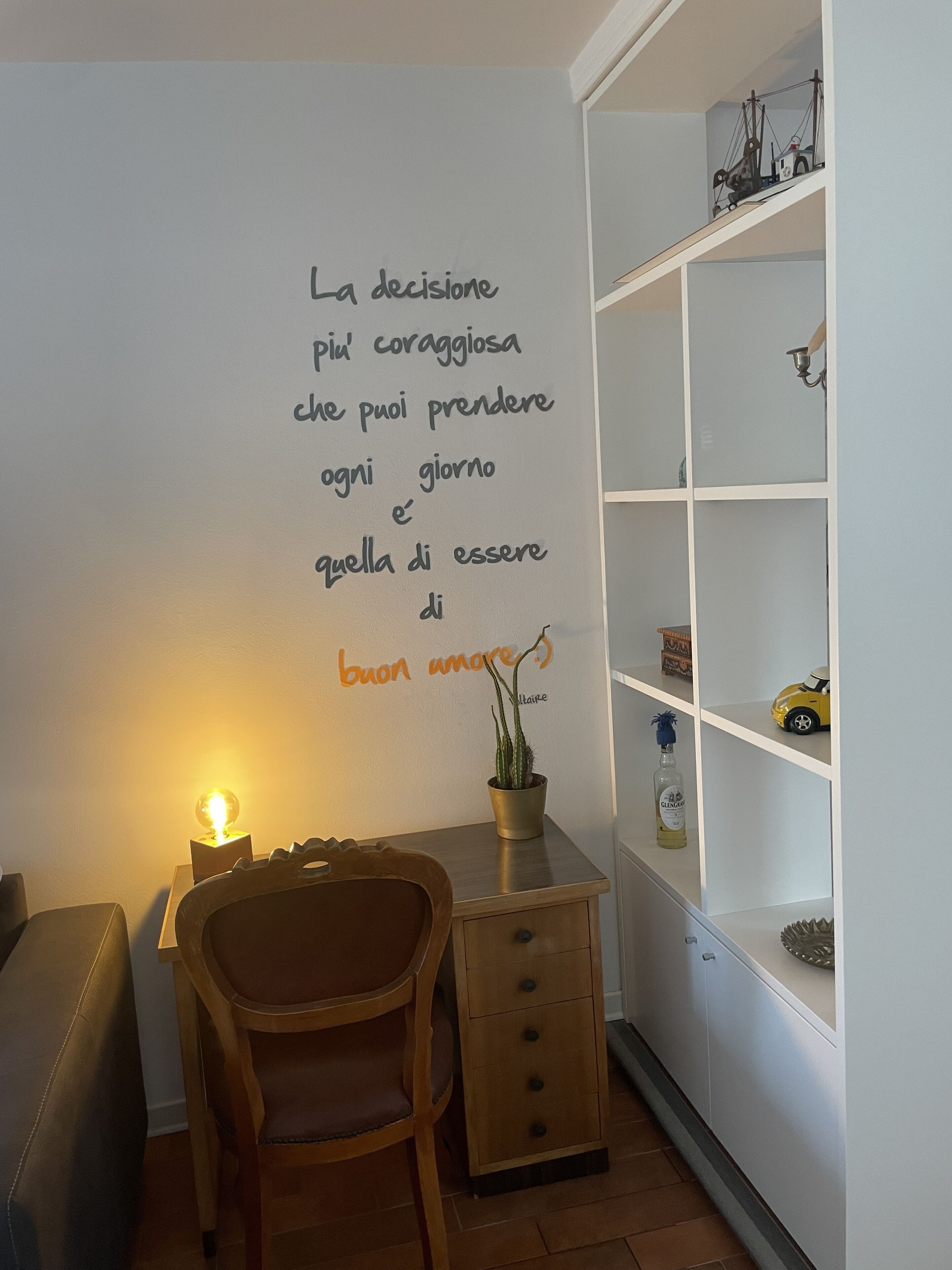 Une pièce chaleureuse avec une chaise en bois, un petit bureau et une étagère ornée d’objets décoratifs.