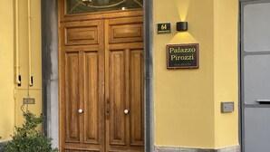 Puinen pariovet, joiden yläosassa on lasiruutu, seinässä oleva kyltti, jossa lukee ”Palazzo Pirozzis”, ja pieni numerokyltti, jossa on numero ”64”.