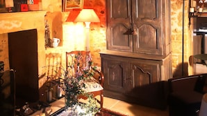 Une pièce rustique avec des poutres apparentes, un meuble ancien, une table avec un livre et une lampe.