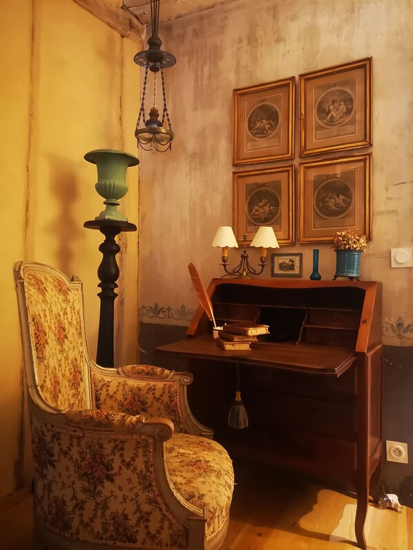 A vintage room with a floral-patterned armchair, a wooden desk with books, a green lamp, and framed pictures on the wall. - Lovely, luxuriously decorated house, intimate garden in a historic village (Le Buisson-de-Cadouin)