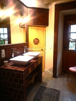 A bathroom with a double sink, a mirror, and a wooden door with a circular decoration. - Lovely, luxuriously decorated house, intimate garden in a historic village (Le Buisson-de-Cadouin)