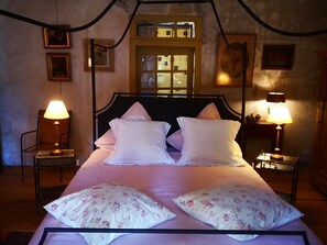 A bed with white linens and floral pillows, flanked by two bedside tables with lamps, in a room with a wooden headboard and a window with a view. - Lovely, luxuriously decorated house, intimate garden in a historic village (Le Buisson-de-Cadouin)