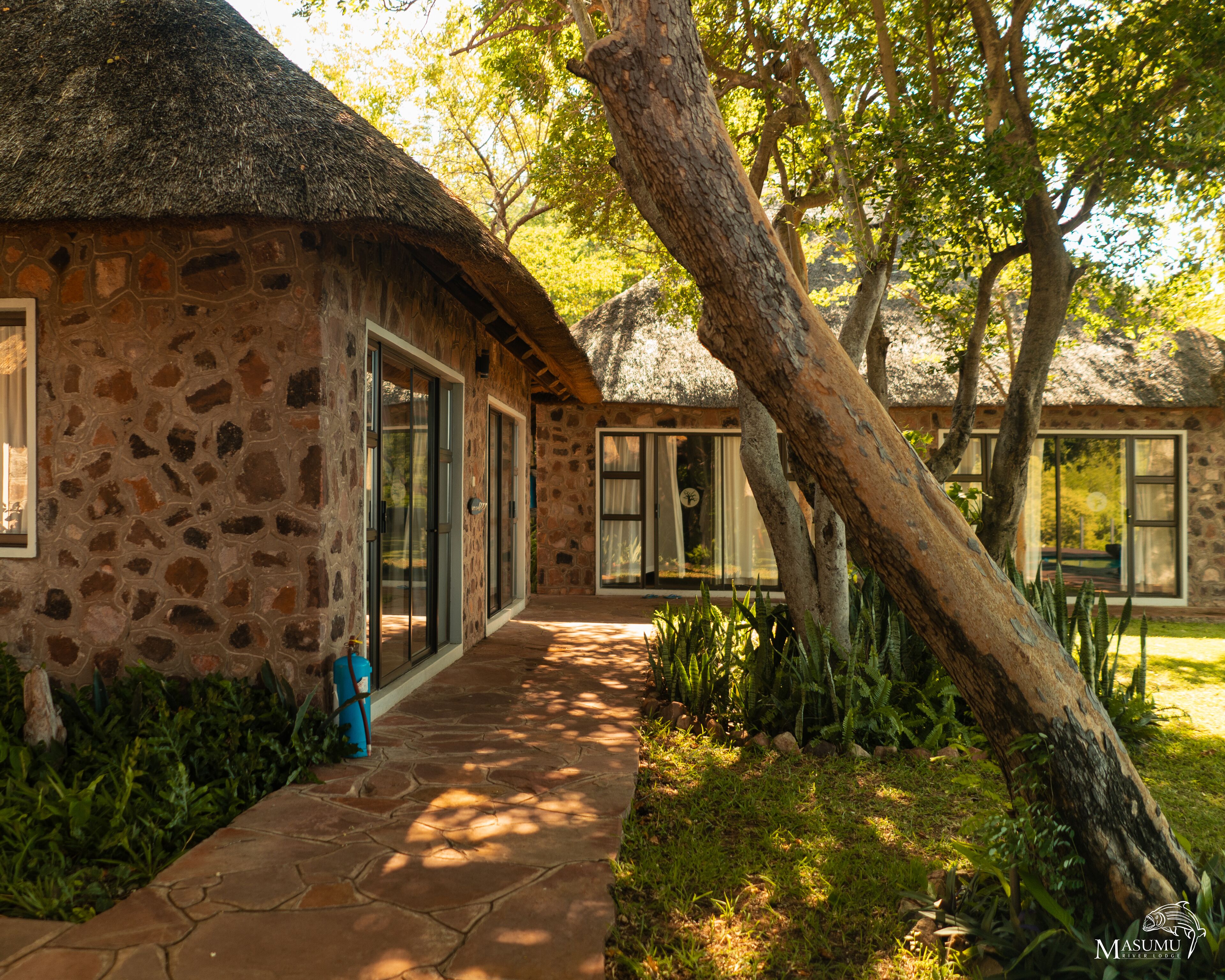 A stone building with a thatched roof, large windows, and a stone pathway leading to the entrance.