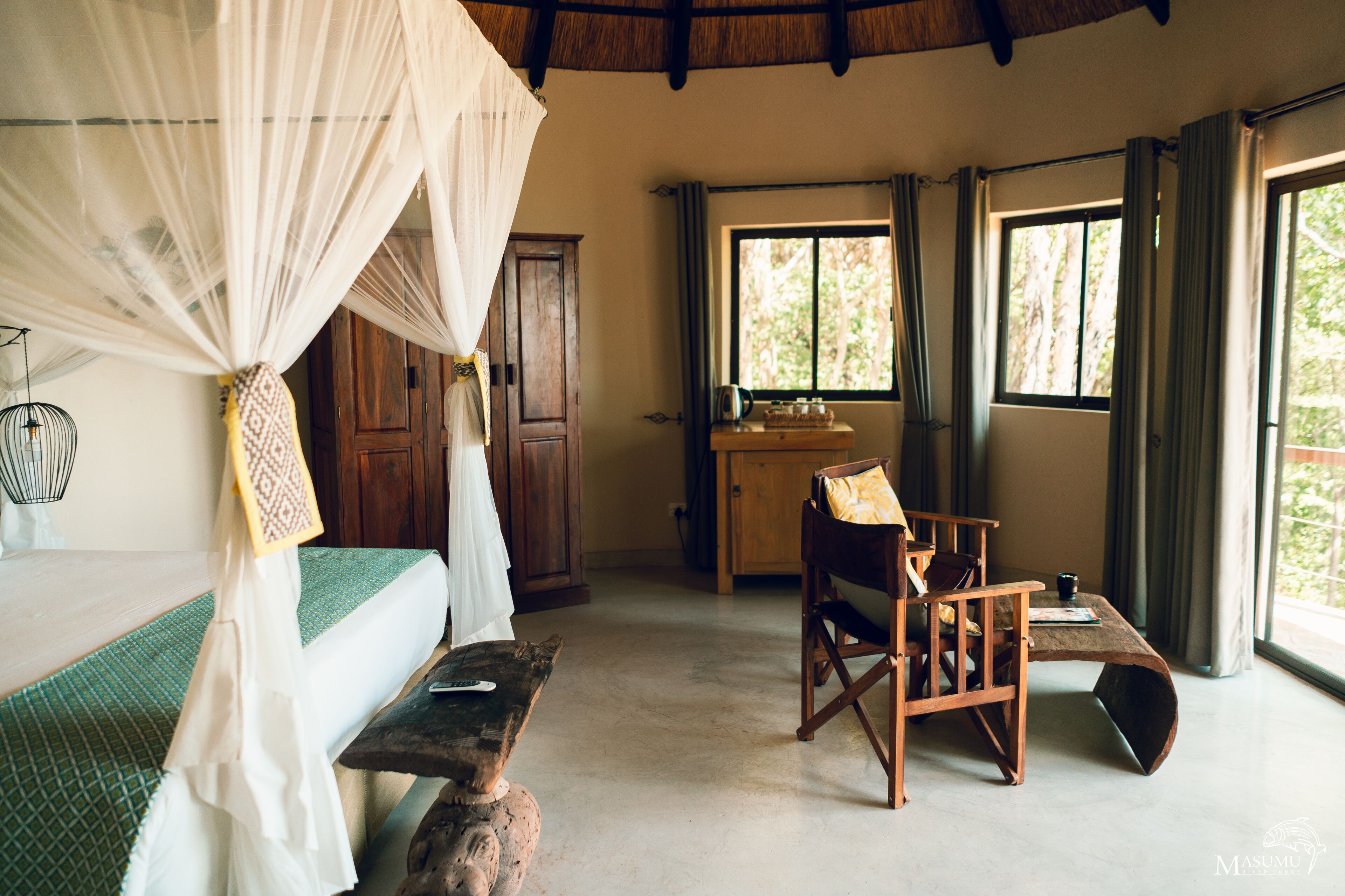 A room with a bed under a canopy, a wooden desk, a chair, and large windows with curtains.